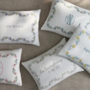 Five decorative pillows with floral embroidery, featuring various names and initials, arranged on a neutral background. Featuring the Daphne Three bedding by Matouk. Available at Linen Society.