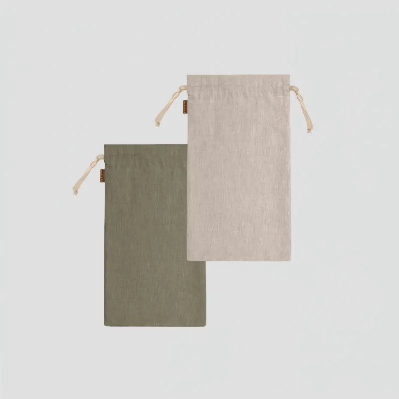A studio laydown of two medium rectangular linen bread bags against a plain light gray background. One bag is olive green and the other is a natural beige color. Both feature natural rope drawstrings and small brown brand tags.