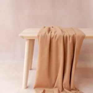 Soft camel cashmere small blanket with fringe by TBCo draped elegantly over a light wooden bench
