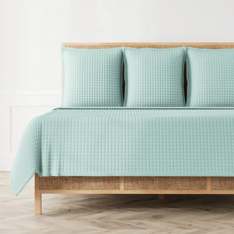 Ann Gish Ready-to-Bed 2.0 quilted coverlet in seafoam, styled on a rattan bed.