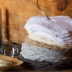 A stack of neatly folded Abyss Habidecor Super Pile Guest Towel Legend sets in neutral tones is arranged on a kitchen counter next to a bar of soap and a sink.